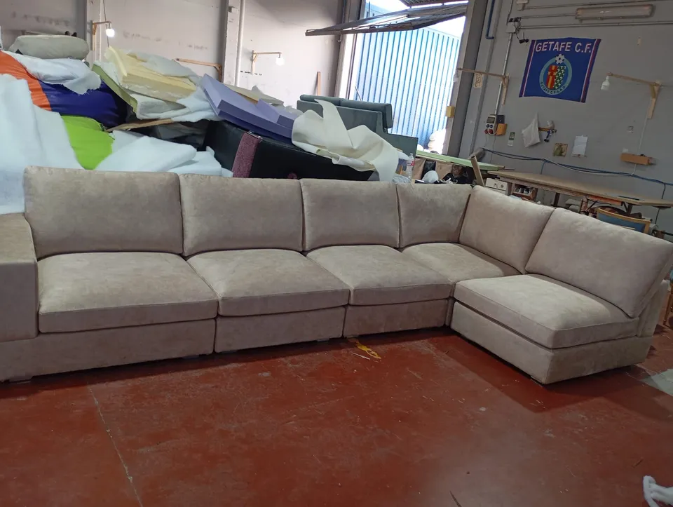 Sofá rinconera con chaise longue tapizado en tela beige, en el taller